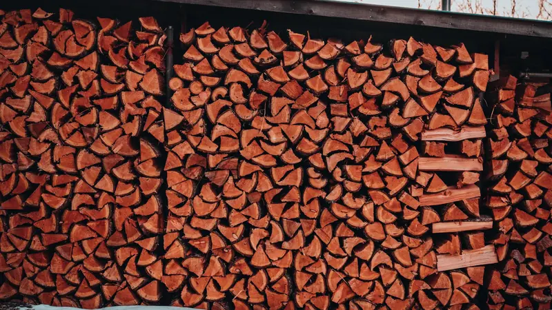 Grand mur de bûches fendues rangées sous l'avancée d'un toit en bois, avec un sol enneigé au premier plan