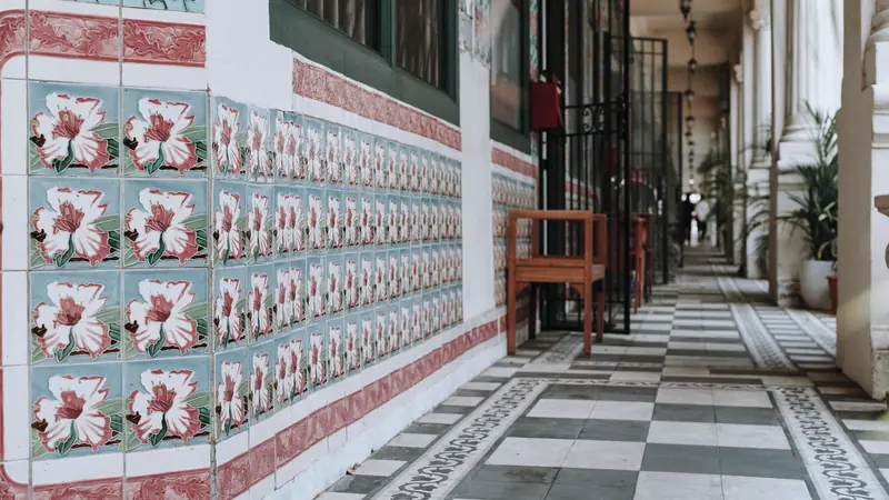 Mur couvert de carreaux décoratifs à fleurs roses sur fond bleu, bordés de frises, le long d'une galerie au sol en damier