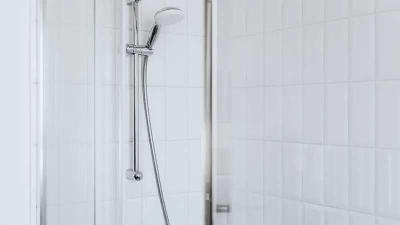 Douche murale chromée devant un carrelage blanc vertical, bordé d'un profilé métallique le long de la paroi vitrée