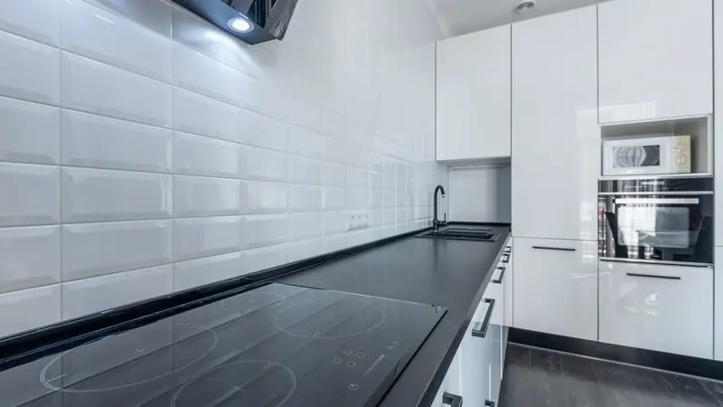 Cuisine blanche avec une crédence en carreaux blancs biseautés posés en quinconce, une plaque à induction noire et une hotte noire