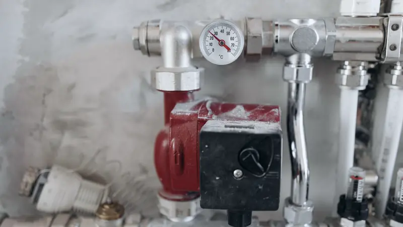 Circulateur rouge et thermomètre à aiguille sur des tuyaux chromés d'un circuit de chauffage