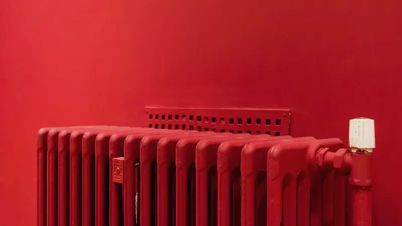 Radiateur en fonte peint en rouge avec sa tête thermostatique blanche, devant un mur rouge