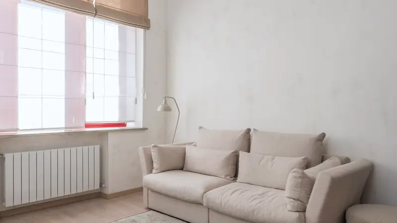Salon clair avec un radiateur blanc à éléments sous la fenêtre et un canapé beige