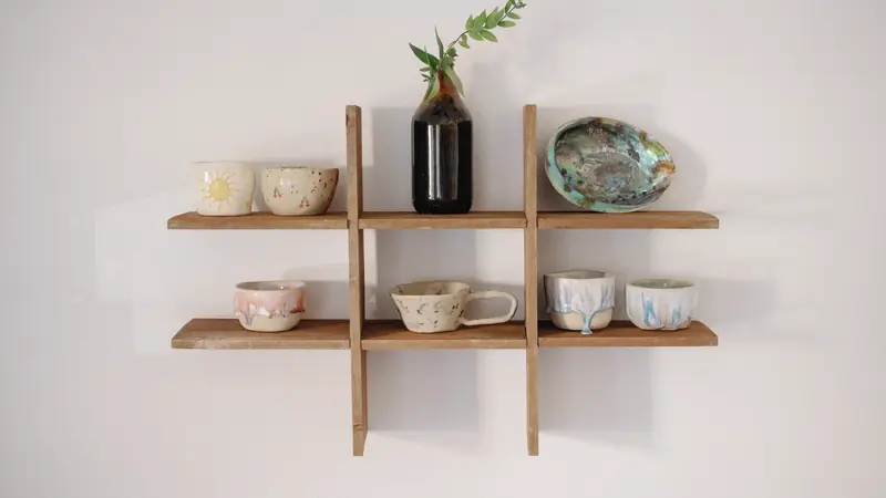 Étagère murale en bois à deux niveaux portant des bols en céramique et un vase avec une branche verte, sur un mur blanc