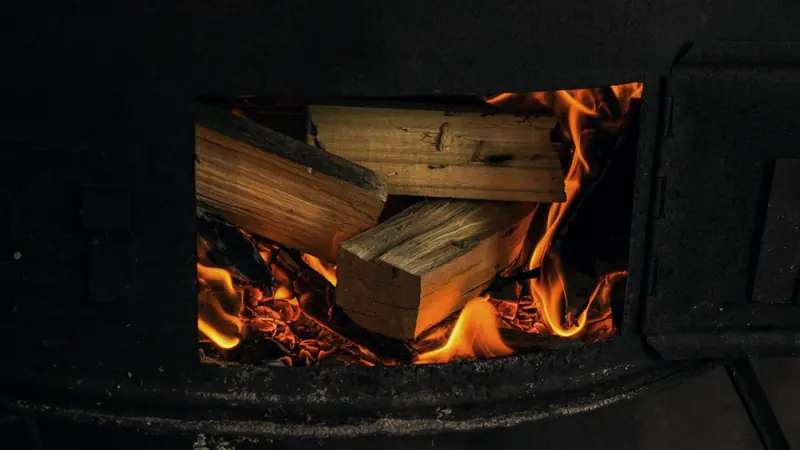 Bûches fendues qui brûlent sur un lit de braises dans le foyer d'un poêle en métal noir