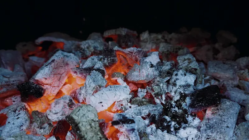 Braises rougeoyantes recouvertes de cendre blanche au fond d'un foyer