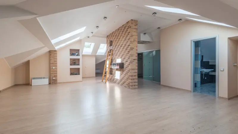 Combles aménagés sous rampants blancs, éclairés par des fenêtres de toit, avec parquet clair et cloison en briques