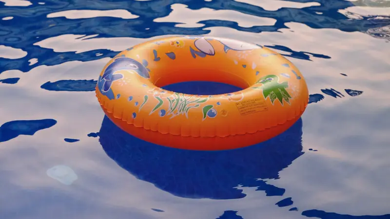 Bouée orange pour enfant décorée d'animaux marins, avec une mention d'avertissement imprimée, flottant sur une eau bleue