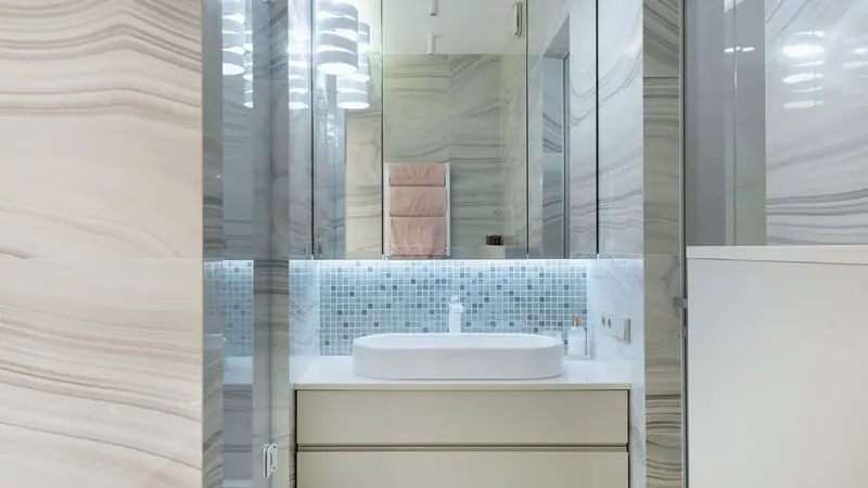 Vasque ovale blanche posée sur un meuble à deux tiroirs crème, crédence en mosaïque et armoire à miroir