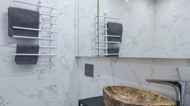 Toilettes au mur de marbre blanc avec une cuvette blanche et une vasque en pierre posée sur une console noire, robinet chromé haut