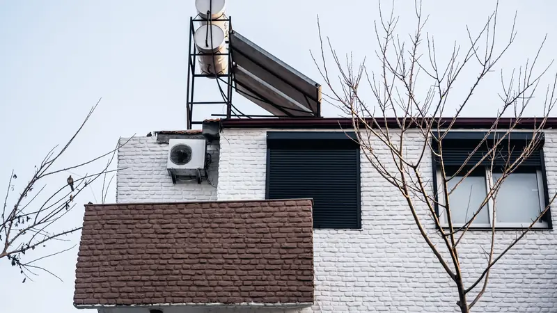 Façade de briques blanches avec une unité extérieure fixée au mur et un chauffe-eau solaire installé sur le toit