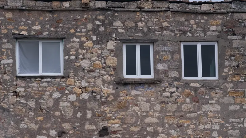 Mur de maison ancienne en pierres apparentes percé de trois fenêtres neuves à cadre blanc