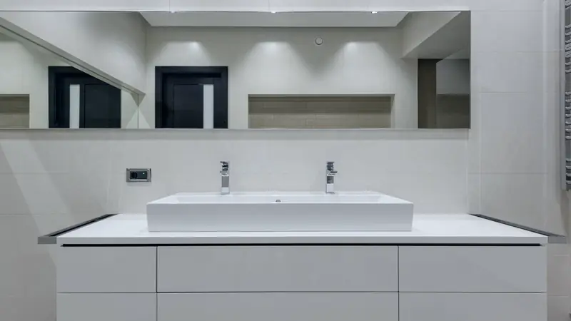 Meuble suspendu blanc à tiroirs portant une longue vasque rectangulaire à poser équipée de deux robinets