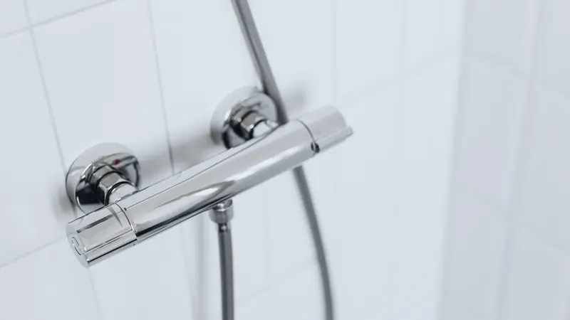 Mitigeur thermostatique chromé et flexible de douche fixés sur un mur carrelé blanc
