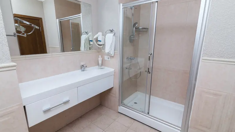Cabine de douche avec receveur blanc, porte coulissante vitrée et murs carrelés beige, à côté d'un meuble vasque