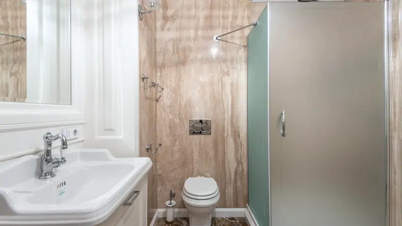Petite salle de bain aux murs habillés de grandes plaques effet marbre beige, avec cabine de douche à porte dépolie