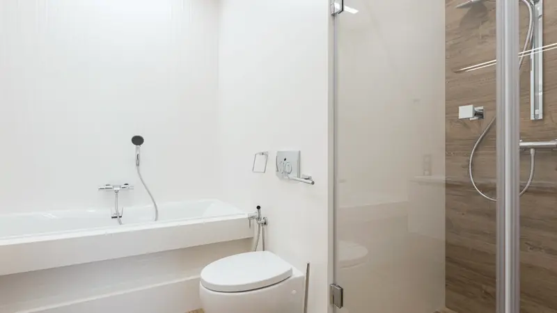 Salle de bain avec baignoire et murs en grands panneaux blancs, douche vitrée sur fond effet bois