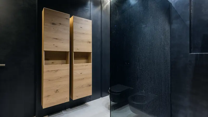 Salle de bain aux murs noirs mats, douche à paroi vitrée et deux colonnes de rangement en chêne suspendues