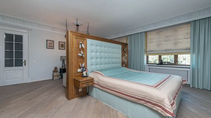 Chambre au parquet de chêne grisé à lames larges, avec un grand lit et une tête de lit en bois