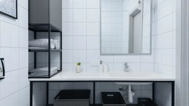 Salle de bain aux murs de carreaux blancs, avec miroir, plan vasque blanc et étagère métallique noire