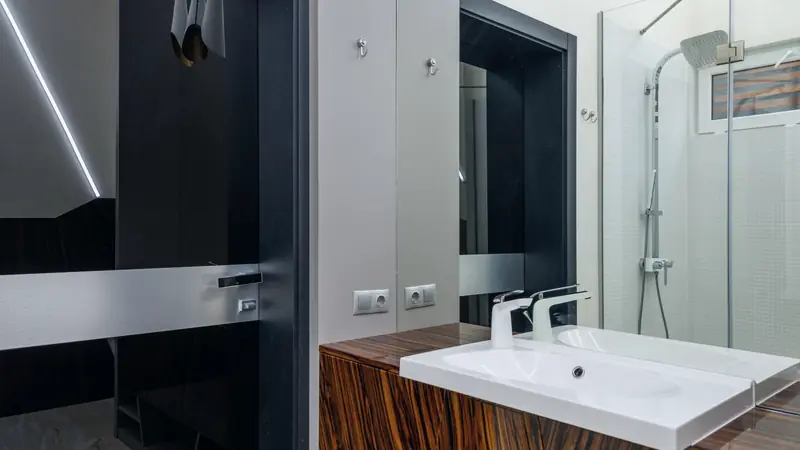 Meuble vasque en bois veiné avec plan vasque blanc et mitigeur, devant une douche à paroi vitrée