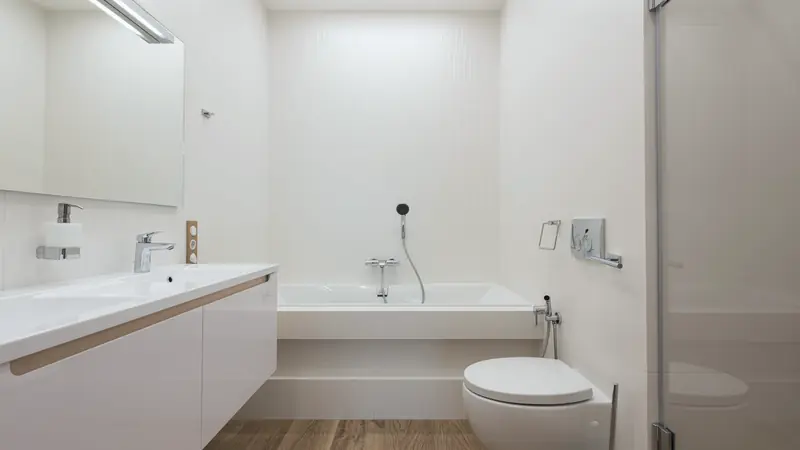 Meuble suspendu blanc à plan vasque, sol imitation bois et baignoire au fond d'une salle de bain claire
