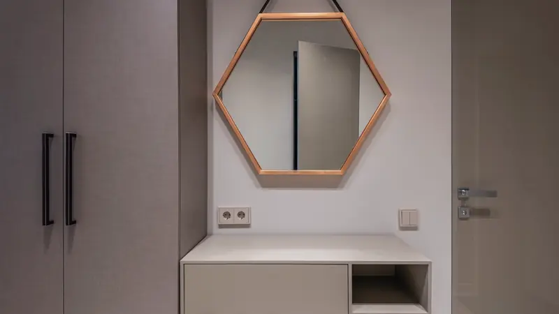 Console blanche à tiroir et niche ouverte sur piètement métallique fin, sous un miroir hexagonal à cadre cuivré