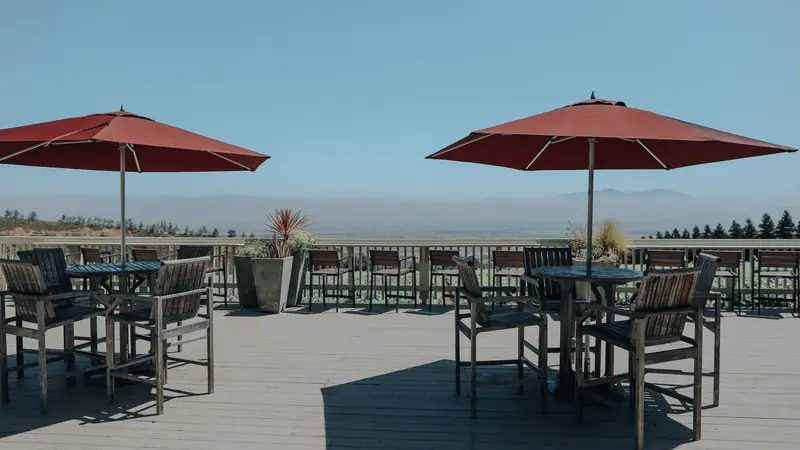 Deux parasols rouges ouverts au-dessus de tables et chaises en bois sur une terrasse en planches