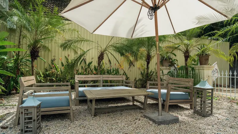 Grand parasol blanc à baleines en bois planté dans un socle carré en pierre sombre, au-dessus d'un salon de jardin sur gravier