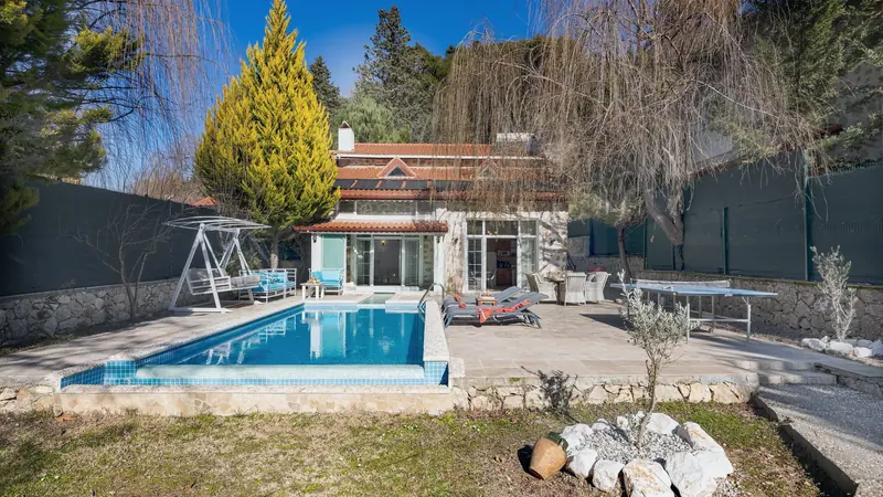 Piscine enterrée devant une maison, sans barrière autour du bassin, dans un jardin fermé par une haute clôture