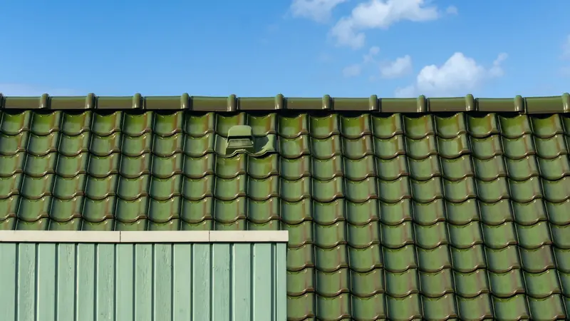 Toit en tuiles vernissées vertes sous un ciel bleu, avec une tuile de ventilation à capot intégrée dans la couverture
