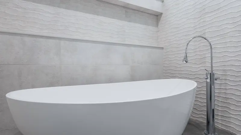 Baignoire îlot blanche de forme ovale et robinet colonne chromé devant un mur en carrelage à relief