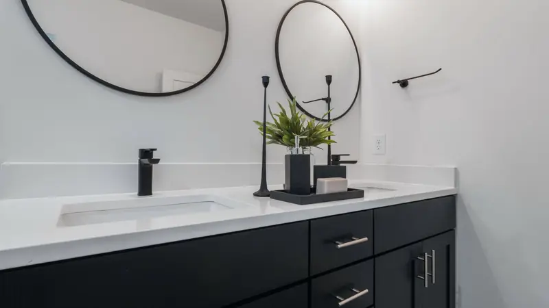 Meuble de salle de bain noir à plan blanc avec deux vasques encastrées, mitigeurs noirs et deux miroirs ronds