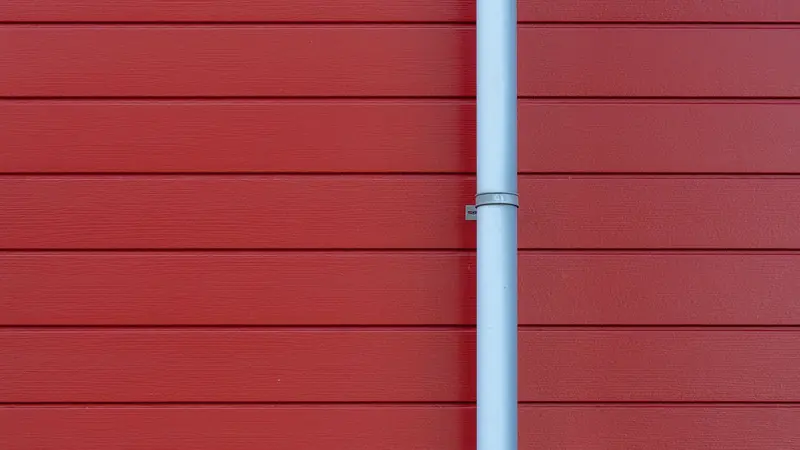 Tuyau métallique gris clair fixé par un collier sur un bardage rouge à lames horizontales