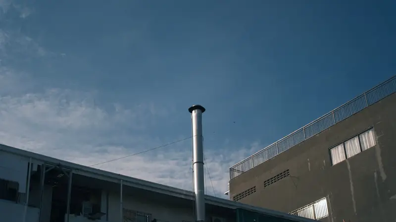 Conduit de fumée métallique avec chapeau, dressé au-dessus des toits sous un ciel bleu